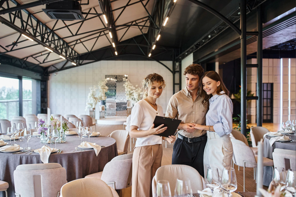 Happy couple looking at contract on clipboard in a wedding venue with a wedding planner.