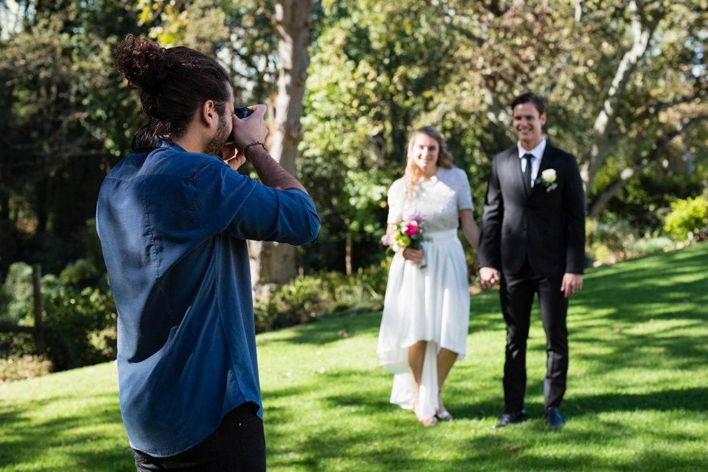 Photographer captures a smiling bride and groom holding hands in a sunlit garden, creating a joyful outdoor wedding portrait.